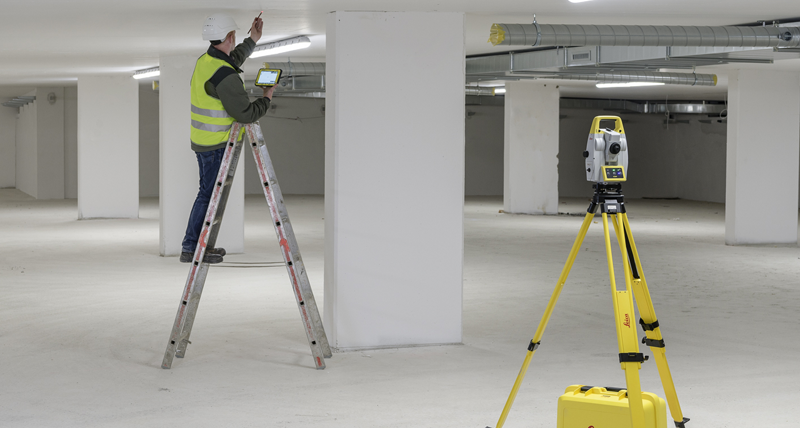 Un spécialiste MEP/CVC sur une échelle marque des points au plafond pendant que l’instrument d’implantation Leica iCON iCT30 tourne automatiquement et met en évidence la position du point avec le faisceau laser